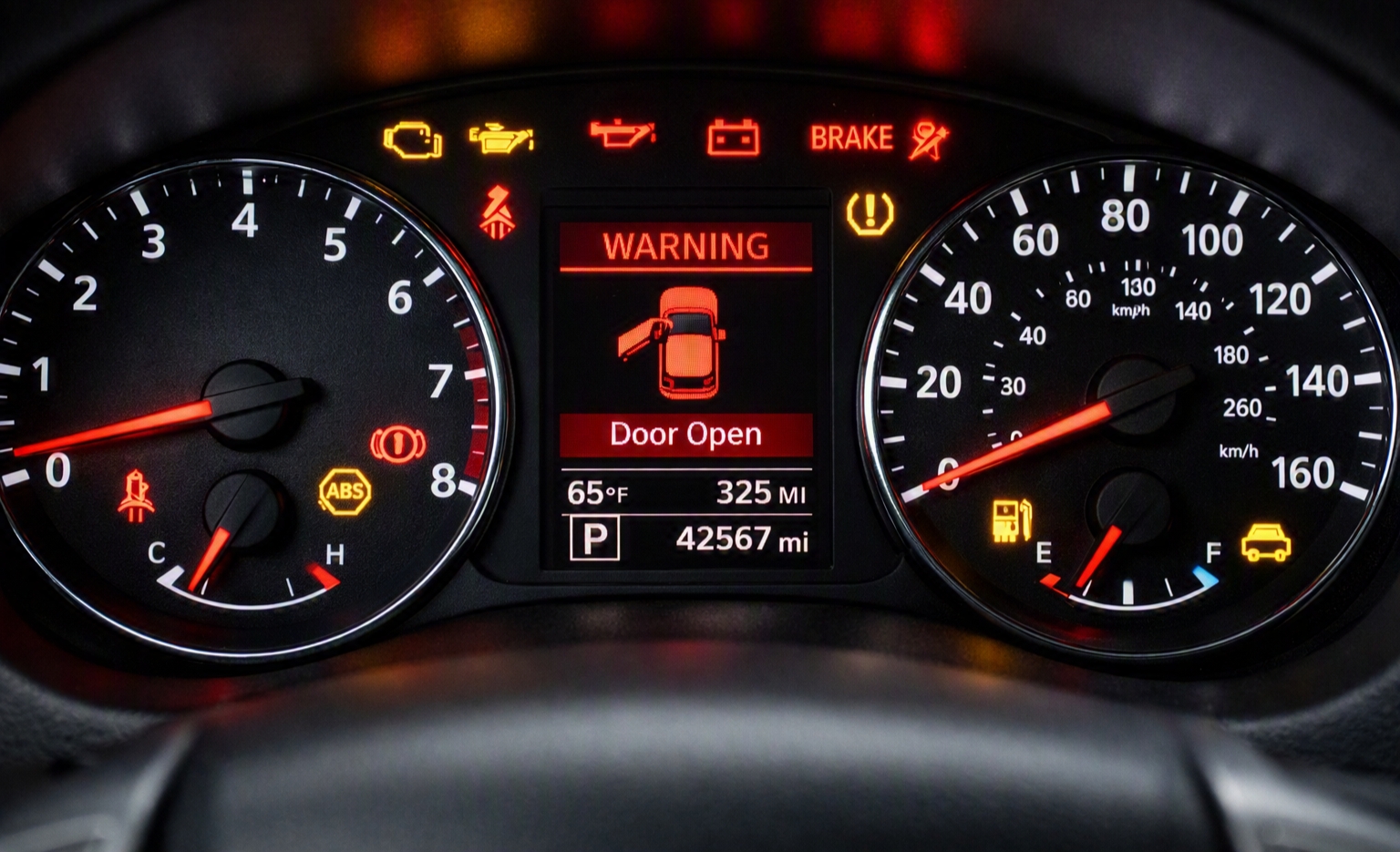 Car dashboard instrument cluster lit up with multiple warning lights including engine, oil pressure, battery, brake and a door open warning message