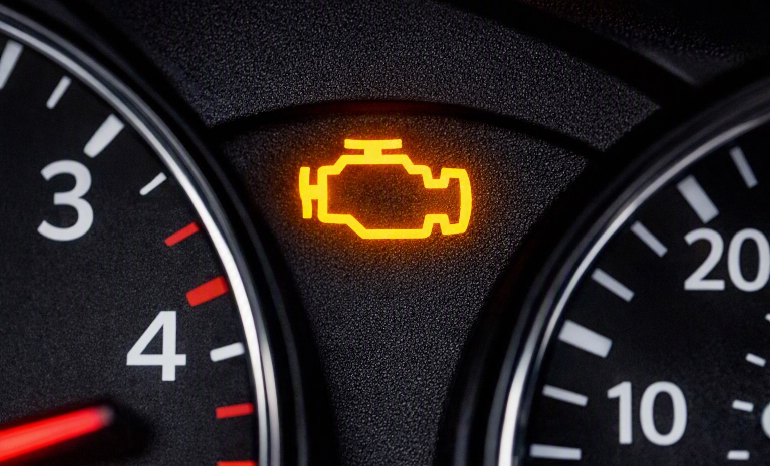 Close-up of an amber engine management warning light illuminated on a car dashboard instrument cluster