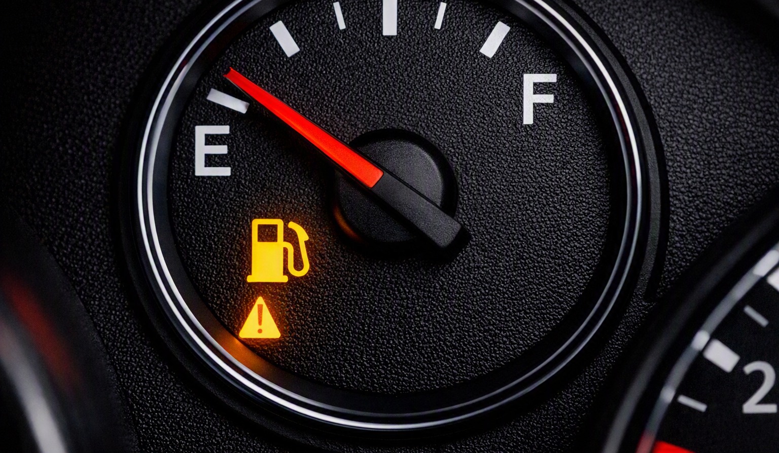 Car fuel gauge showing a near-empty tank with the low fuel warning light illuminated